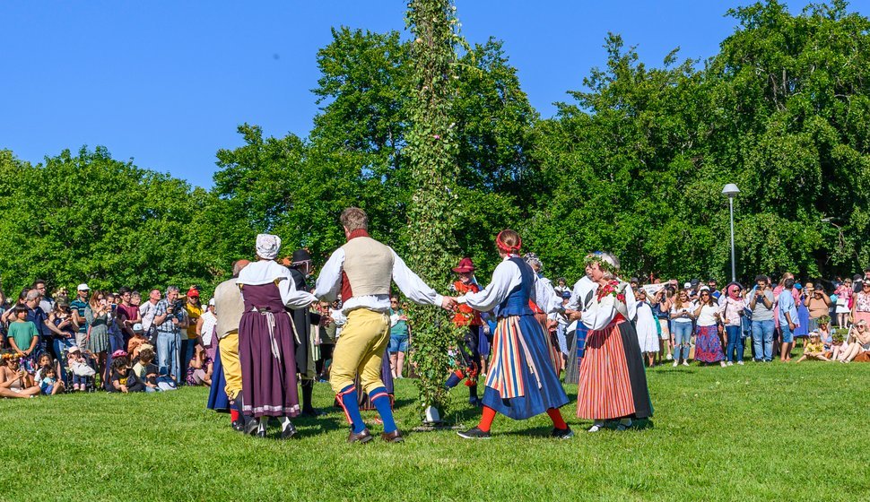 Klädda deltagare dansar runt midsommarstången. 2022, Vaxholm, Stockholm.